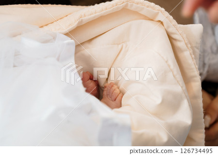 A close-up view of a newborn baby's tiny feet peeking out from under a soft, cream-colored blanket, representing the tenderness and vulnerability of new life A close-up view of a newborn baby's tiny feet peeking out from under a soft, cream-colored blanket, representing the tenderness and vulnerability of new life 126734495