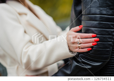 A couple embracing outdoors, a woman with red nails and a silver ring resting her hand on a man in a black leather jacket, suggesting romance and affection A couple embracing outdoors, a woman with red nails and a silver ring resting her hand on a man in a black leather jacket, suggesting romance and affection 126734511
