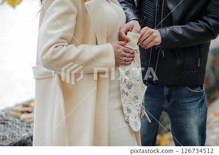 A tender moment featuring a pregnant woman in a cream coat and her partner holding a small baby pacifier outdoors in autumn, symbolizing anticipation of parenthood 126734512