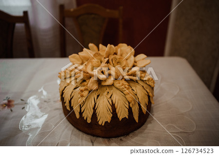 Rustic traditional Italian Panettone cake decorated with intricate pastry flowers sits prominently on a lace-covered table in a warmly lit dining room setting, evoking a sense of home Rustic traditional Italian Panettone cake decorated with intricate pastry flowers sits prominently on a lace-covered table in a warmly lit dining room setting, evoking a sense of home 126734523