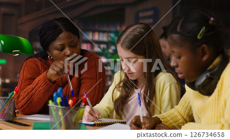 Female teacher assisting pupils with class homework and mentoring, providing academic instruction and support to help pass school assignments. Tutor lecturer gives private lessons. Camera B. 126734658
