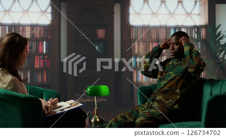 Black combat veteran faces grief and trauma crying at therapy session, addressing PTSD and talking about combat scenes. Sad shocked soldier shares war flashbacks with counselor. Camera B. 126734702