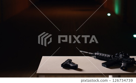 Practice weapons in military training outpost to be used by soldiers learning how to shoot firearms at paper target. Close up of pistol and rifle in army shooting range used for hitting bullseye 126734739