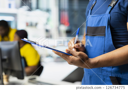 Technician investigating malfunctioning systems in photovoltaics factory, comparing parameters with pc and files. Black employee inspecting solar panels manufacturing plant, high tech. 126734775