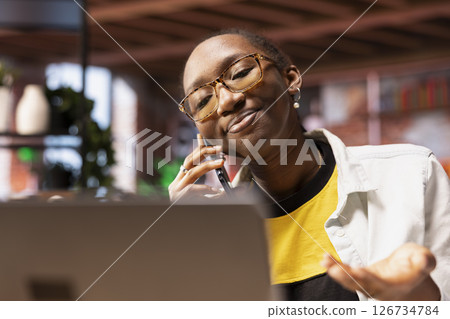 Upbeat woman having friendly conversation with friends during telephone call using smartphone. Happy african american person having fun catching up with mates, talking on phone 126734784