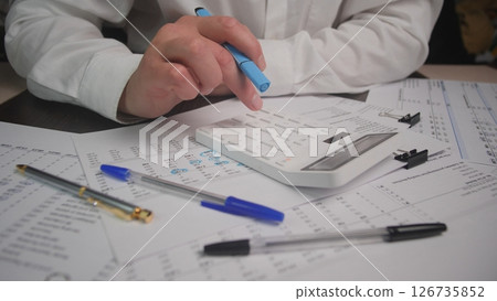 Business Professional Calculating Finances With a Calculator, Notes, and Pens on a Desk During Work Hours at an Office 126735852