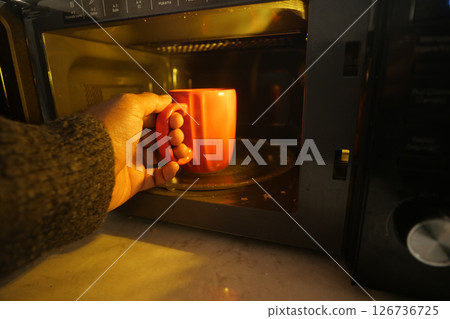 Hand holding red mug while using microwave at home 126736725