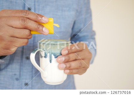 young man putting artificial sweetener into a cup of tea on table . young man putting artificial sweetener into a cup of tea on table . 126737016