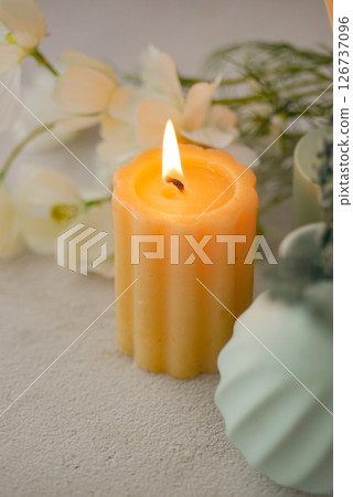 Decorative candle with flame and flowers on light surface Decorative candle with flame and flowers on light surface 126737096