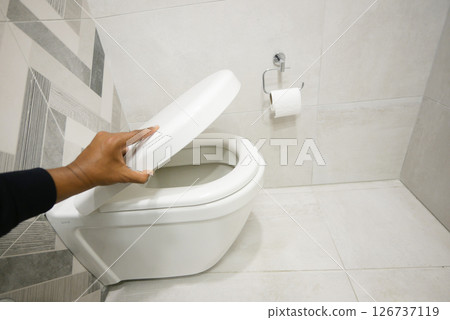 Hand lifting the lid of a clean toilet in a bathroom Hand lifting the lid of a clean toilet in a bathroom 126737119