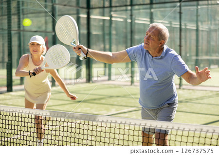 Old man and woman playing Padel Tennis in open-air tennis court 126737575