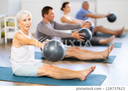 Group of mature people in sportswear exercising Pilates with soft balls while sitting on mats in fitness studio 126737623