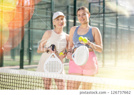 Happy senior woman and her daughter standing in padel court getting ready for match Happy senior woman and her daughter standing in padel court getting ready for match 126737662