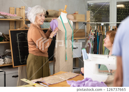 Elderly female teacher showing how to sew on mannequin 126737665