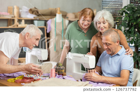 Senior male teacher demonstrates technique sewing with machine, shares skills with elderly students 126737792