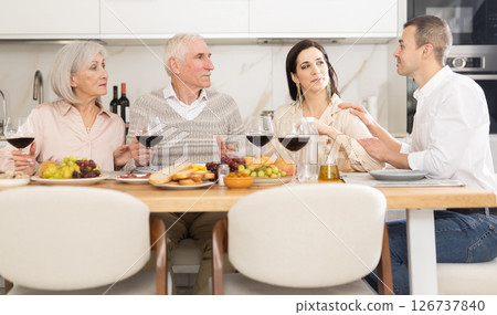 Mature married couple are sitting at table, enjoying food and wine with middle-aged guests. Mature married couple are sitting at table, enjoying food and wine with middle-aged guests. 126737840