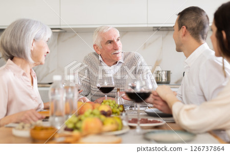 Mature married couple are sitting at table, enjoying food and wine with middle-aged guests. Mature married couple are sitting at table, enjoying food and wine with middle-aged guests. 126737864
