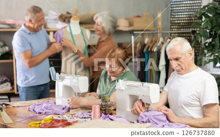 Mature man and woman sew and talking, others senior people work with mannequin at sewing school studio 126737880