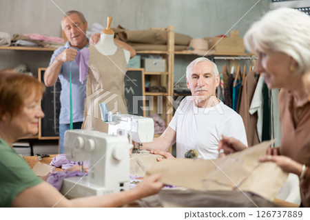 Senior man work with mannequin at sewing school studio, others people sew and talking Senior man work with mannequin at sewing school studio, others people sew and talking 126737889