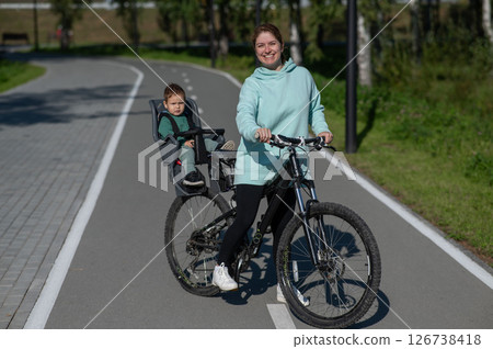 Caucasian woman riding a bicycle with her toddler son sitting behind her in a child seat. Caucasian woman riding a bicycle with her toddler son sitting behind her in a child seat. 126738418