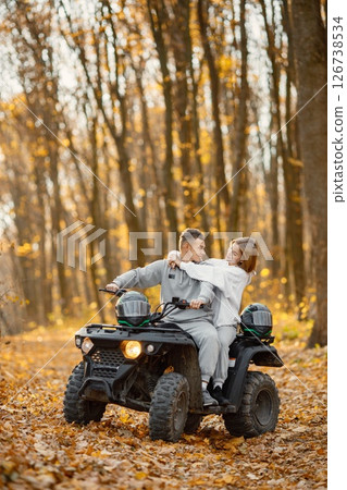 A young caucasian man and woman riding an ATV quad bike in autumn forest. Lovely couple hugging. Couple wearing grey sportive costumes. 126738534