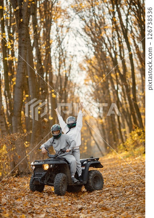 A young caucasian man and woman riding an ATV quad bike in autumn forest. Couple maneuvering off-road ATV. Couple wearing grey sportive costumes. 126738536