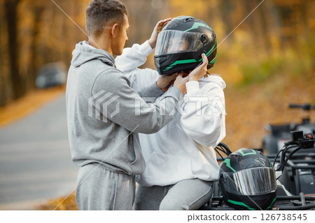 Young caucasian man and woman on an ATV quad bike in autumn forest. Man wearing a helmet on a woman. Couple wearing grey sportive costumes. 126738545