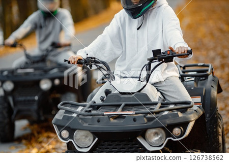 Focus on a woman riding an ATV quad bikes in autumn forest. Two friends maneuvering off-road ATV. Couple wearing grey sportive costumes. Focus on a woman riding an ATV quad bikes in autumn forest. Two friends maneuvering off-road ATV. Couple wearing grey sportive costumes. 126738562