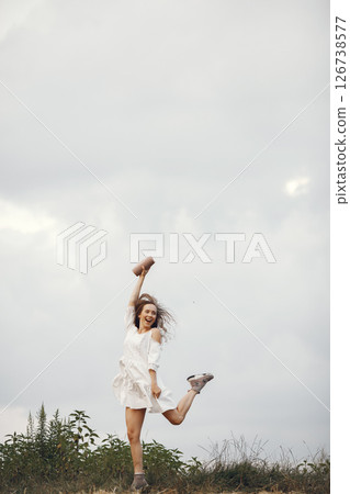 Woman in a summer field. Brunette in a white dress. Girl with music speaker. 126738577