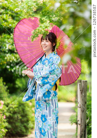 A young woman in a kimono walking through a park with fresh green leaves 126738587