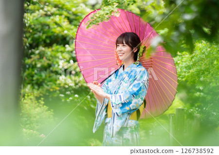 一位身穿和服的年輕女子走過綠葉盛開的公園 126738592