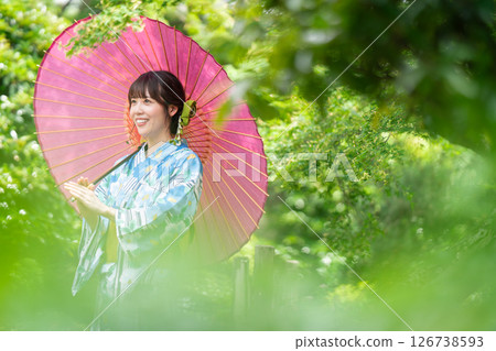 一位身穿和服的年輕女子走過綠葉盛開的公園 126738593
