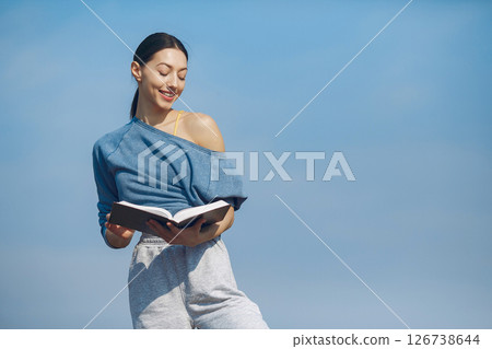 Beautiful girl standing on a sky background. Woman in a blue sweater. Lady with book in her hands Beautiful girl standing on a sky background. Woman in a blue sweater. Lady with book in her hands 126738644
