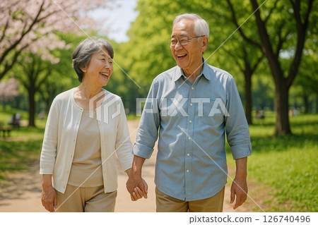 An elderly couple walking hand in hand along a cherry blossom-lined street 126740496