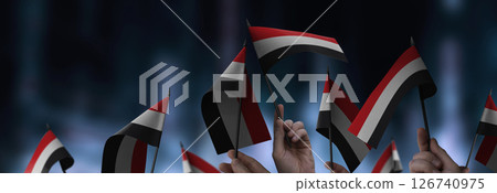 Yemen flags in their hands on a blurred urban background Yemen flags in their hands on a blurred urban background 126740975