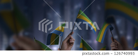Gabon flags in their hands on a blurred urban background Gabon flags in their hands on a blurred urban background 126740993