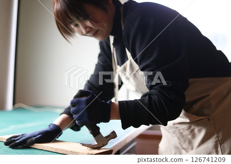A woman removing a nail from a board A woman removing a nail from a board 126741209