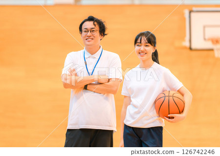 A male teacher and a female student holding a basketball in a gym 126742246