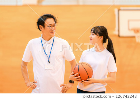 A male teacher and a female student holding a basketball in a gym 126742248