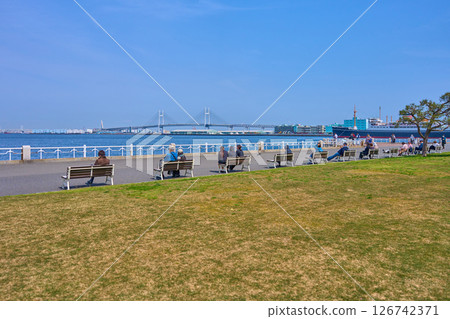 人們在神奈川縣橫濱市山下公園草坪前的長椅上休息，並欣賞海灣大橋的景色 126742371