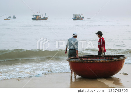 Vietnamese male fishermen with a traditional Vietnamese round basket boat on the beach by the sea in a village in Vietnam 126743705