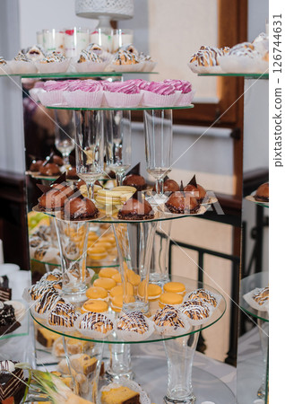 A lavish dessert display featuring tiered glass stands filled with an assortment of colorful cupcakes, chocolate treats, macarons, and champagne glasses at an event 126744631