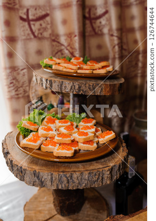 Elegant canapes with red caviar on wooden tiered serving stands in a rustic setting, featuring a natural wood backdrop and refined presentation for a formal event Elegant canapes with red caviar on wooden tiered serving stands in a rustic setting, featuring a natural wood backdrop and refined presentation for a formal event 126744644