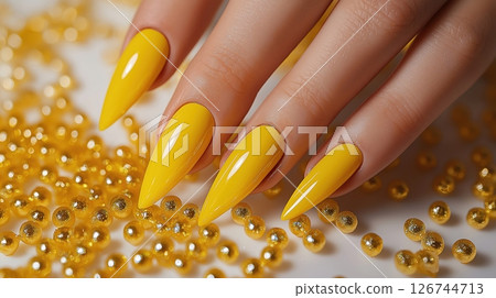 close-up of a woman's hand with long, pointed nails. The nails are painted with a bright yellow polish and have a glossy finish	 126744713