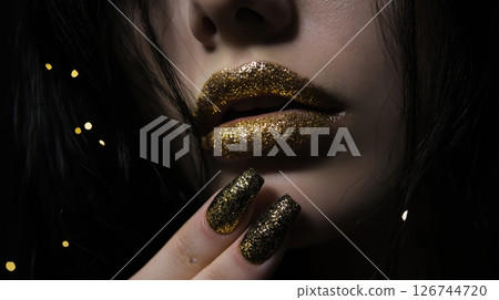 close-up portrait of a woman's face and upper body. The woman has long dark hair and her lips are painted with gold lipstick. Her nails are painted black with gold glitter close-up portrait of a woman's face and upper body. The woman has long dark hair and her lips are painted with gold lipstick. Her nails are painted black with gold glitter 126744720