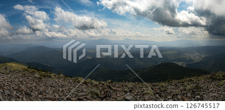 A stunning view of the mountain horizon beneath a bright blue sky dotted with clouds. 126745517