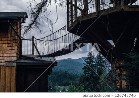 A cozy wooden treehouse, complete with a suspended bridge, blends into the natural surroundings. 126745740