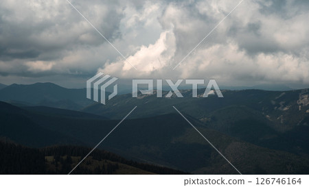 A sweeping view of rolling mountain ranges under a cloud-filled sky. 126746164