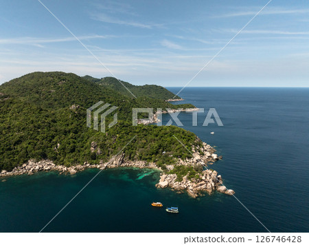 Lush green headland reaching out to calm turquoise waters with a few small boats anchored nearby. Thailand, Koh Tao. 126746428