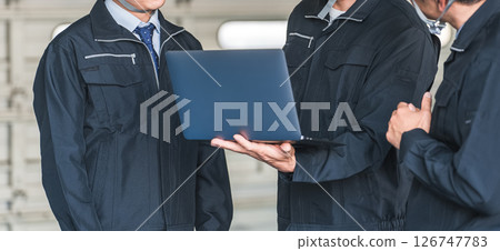 A male worker having a meeting while looking at a computer at a factory, warehouse, or logistics center 126747783